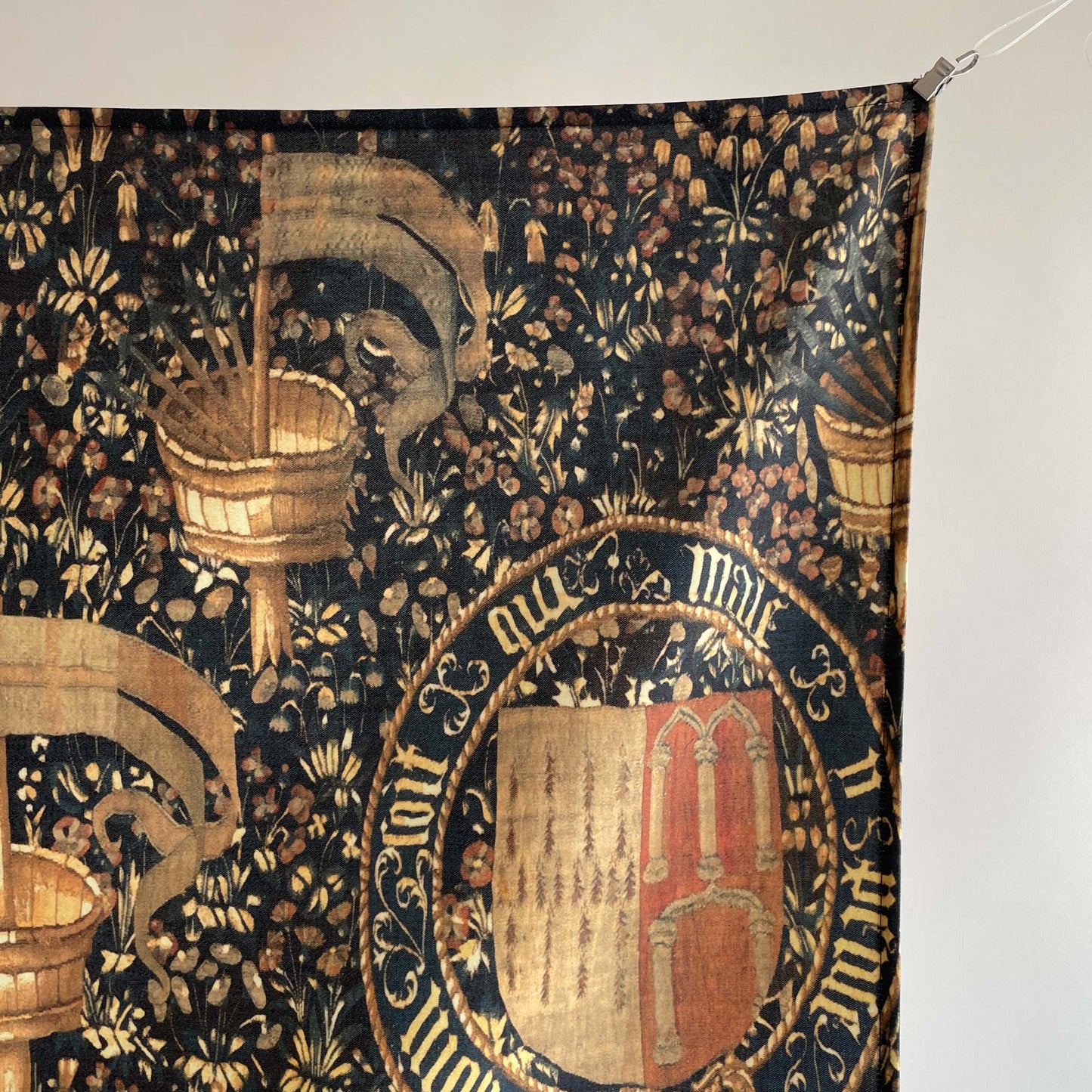 Detailed view of the upper right corner of the Armorial Bearings tapestry, featuring medieval heraldic crest and floral background.