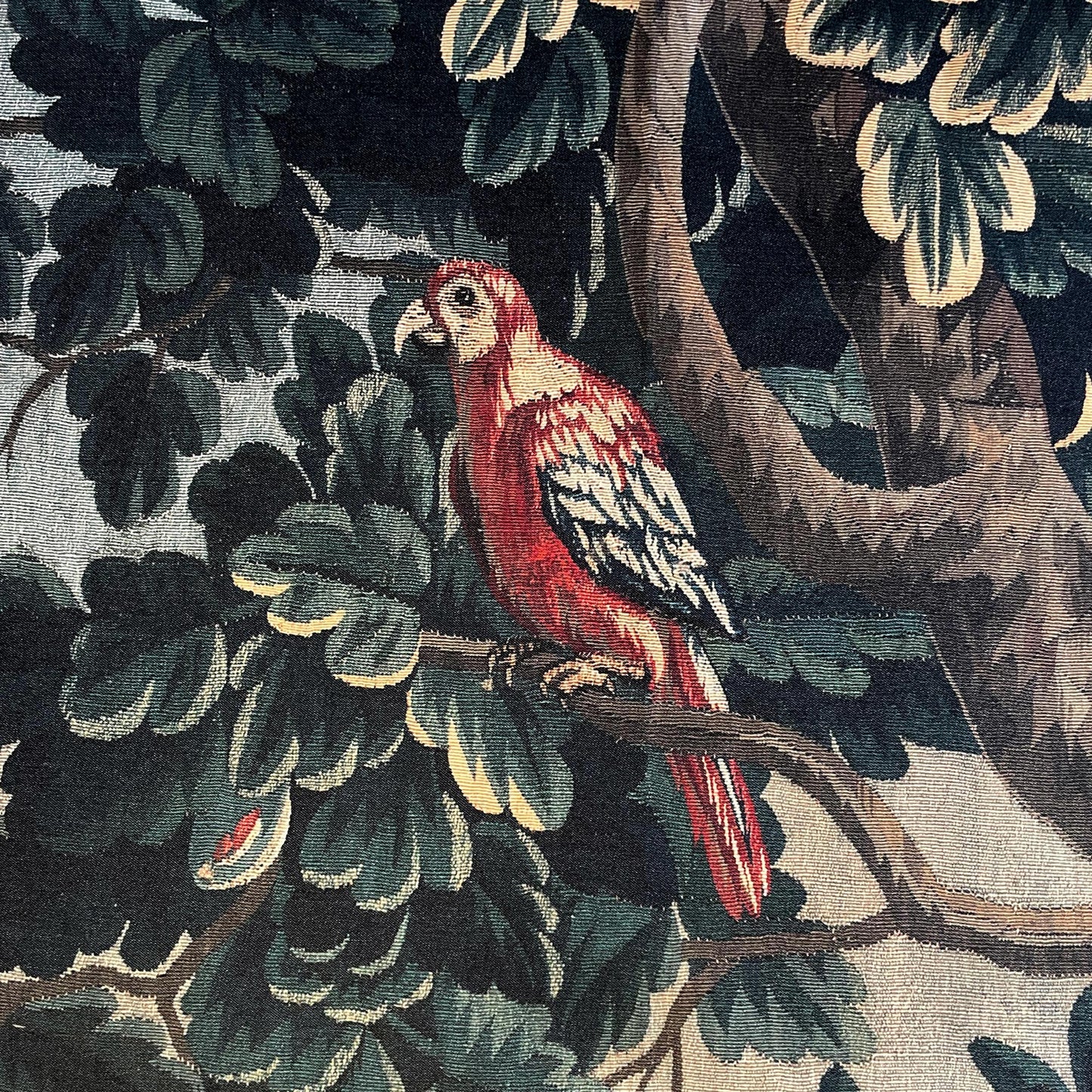 Verdure Chateau Garden tapestry detail with red parrot on a branch, layered leaves, and rich green tones.