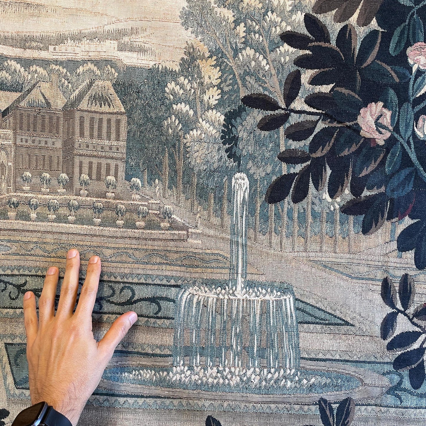 Verdure Chateau Garden tapestry fountain and formal parterres with distant château; hand shows scale and weave.