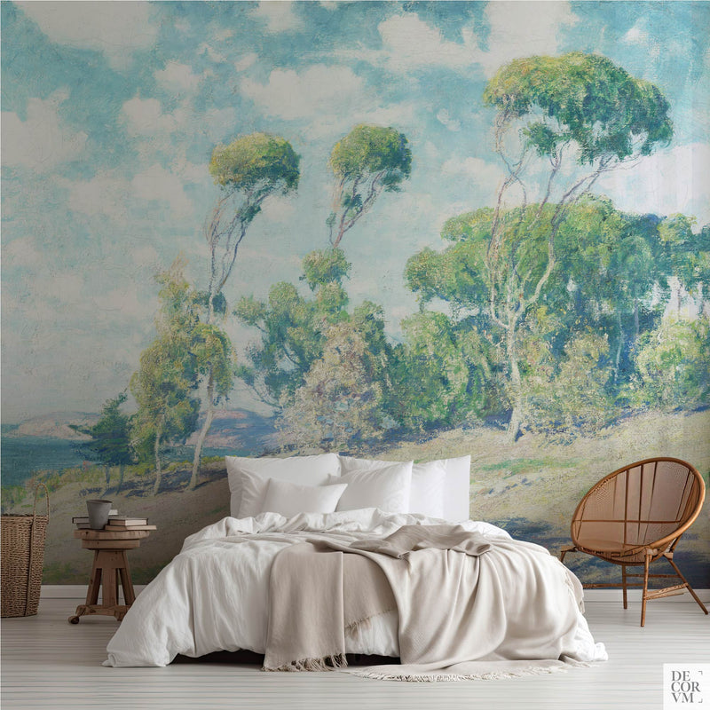 Eucalyptus coastal wallpaper mural in a serene bedroom — California impressionist landscape with sunlit trees behind rattan furniture and white linens by Decorvm
