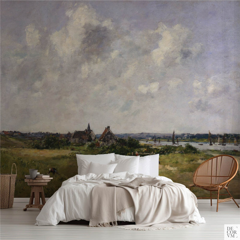 Coastal dunes and sky wallpaper mural of pale dune grass under heavy white cloud, covering the wall behind a low bed with white linens, a wooden stool and a round rattan chair in a soft-neutral bedroom by Decorvm.