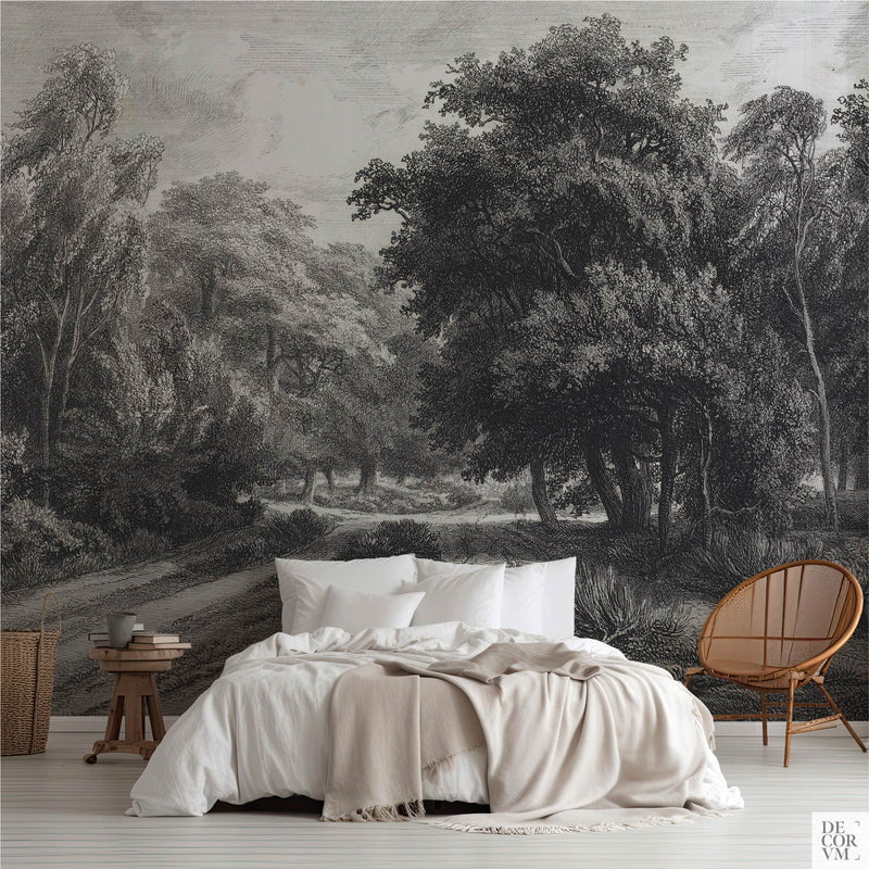 Fontainebleau forest etching wallpaper mural covering the wall behind a low bed with white linens, a wooden stool, and a rattan chair in a soft-neutral bedroom by Decorvm.