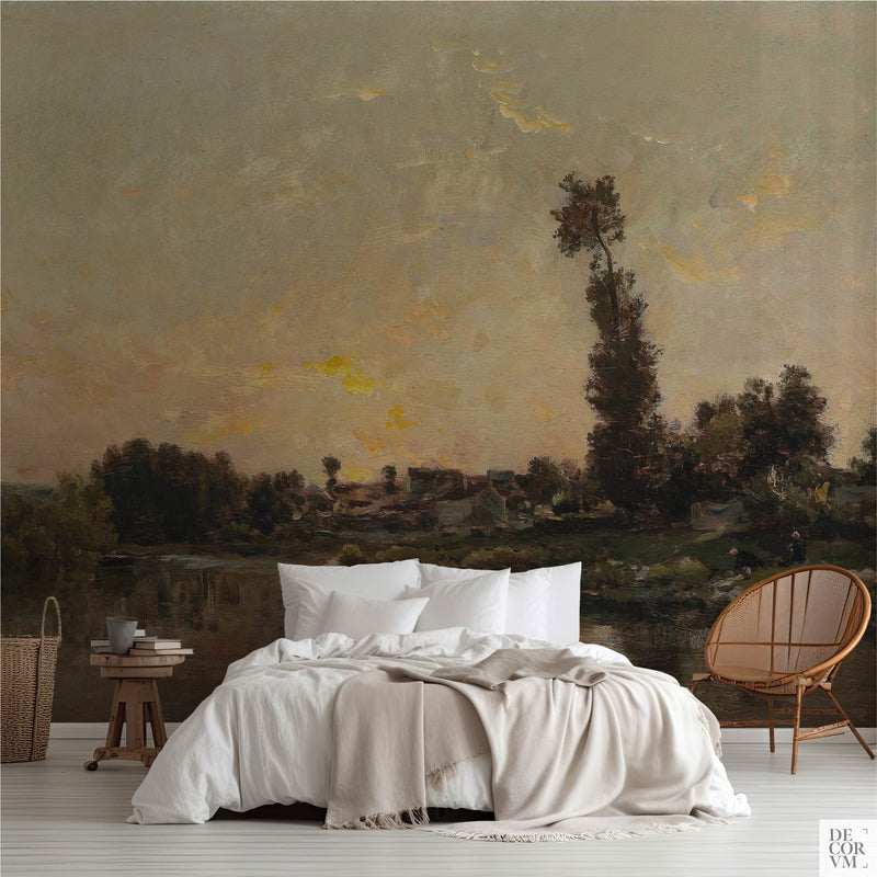 Golden river sunset wallpaper mural of an apricot sky over the Oise, covering the wall behind a low bed with white linens, a wooden stool and a round rattan chair in a soft-neutral bedroom by Decorvm.