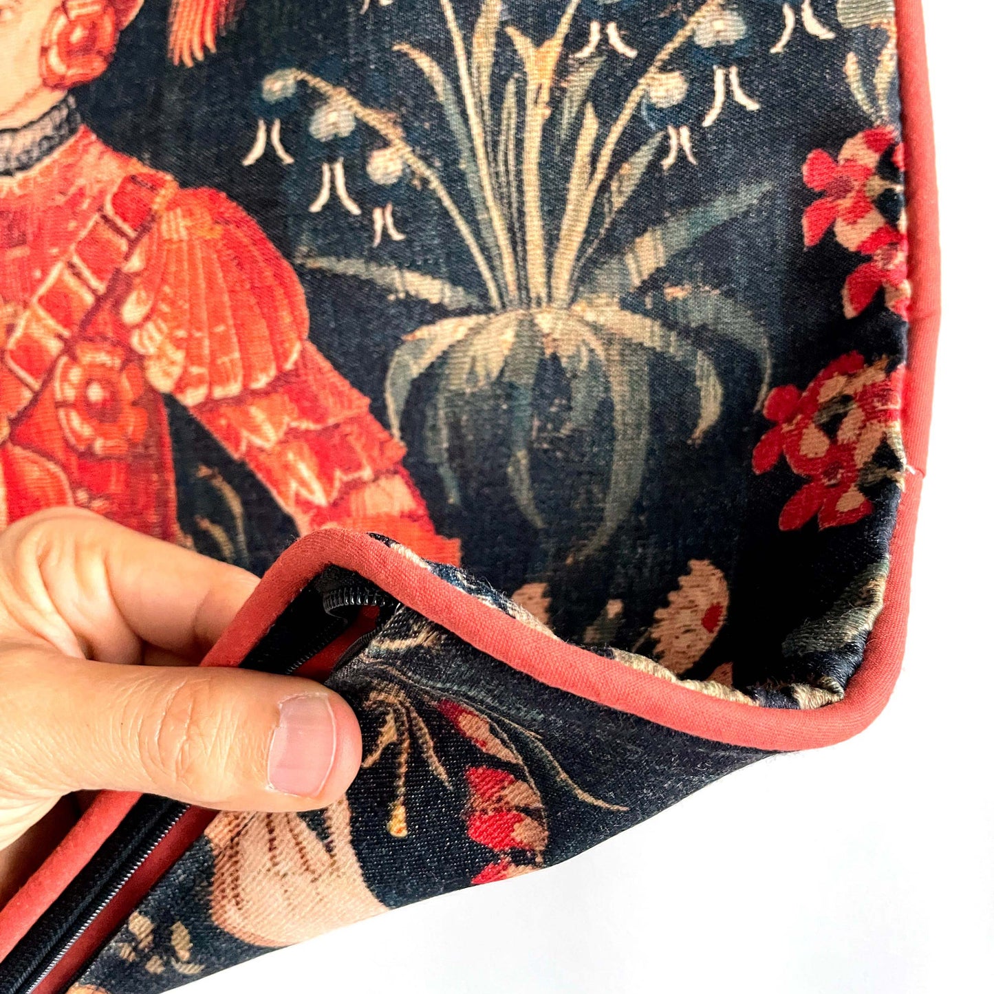 A hand opening the hidden zipper on the Medieval Amazon Queen cushion cover, showing the high-quality construction and red piping detail.