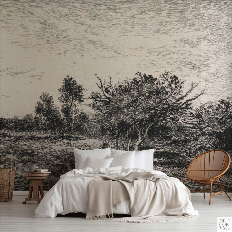 Monochrome tree etching wallpaper mural covering the wall behind a low bed with white linens, a wooden stool, and a rattan chair in a soft-neutral bedroom by Decorvm.
