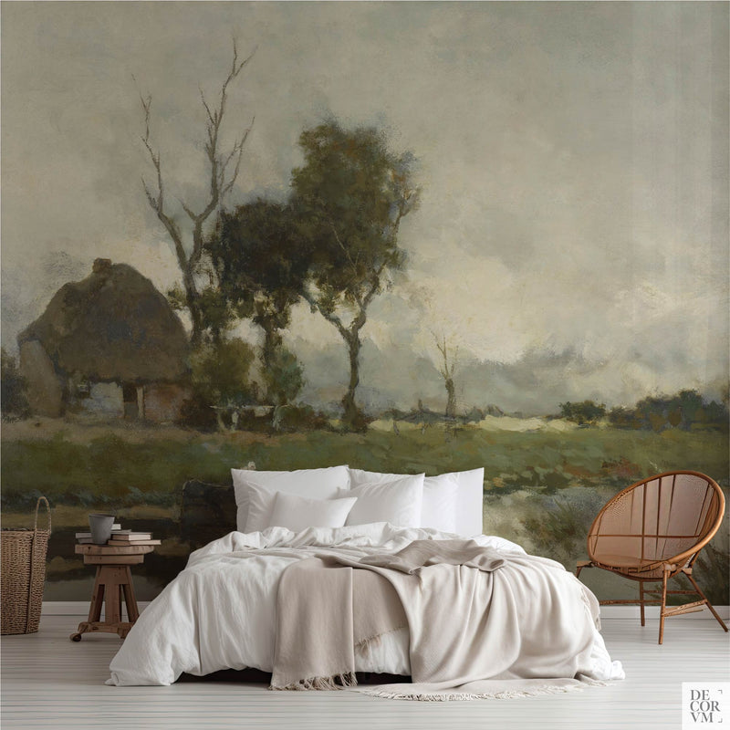 Moody grey green wallpaper mural of a towering pale sky over flat Dutch country, covering the wall behind a low bed with white linens, a wooden stool and a round rattan chair in a soft-neutral bedroom by Decorvm.