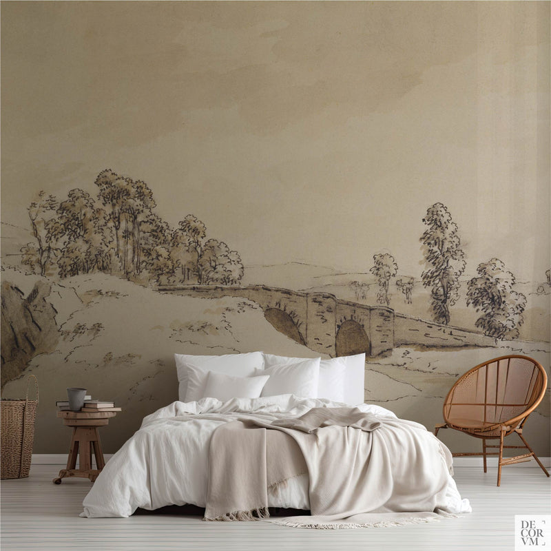 Sepia bridge drawing wallpaper mural of an antique ink landscape sketch, covering the wall behind a low bed with white linens, a wooden stool and a round rattan chair in a soft-neutral bedroom by Decorvm.