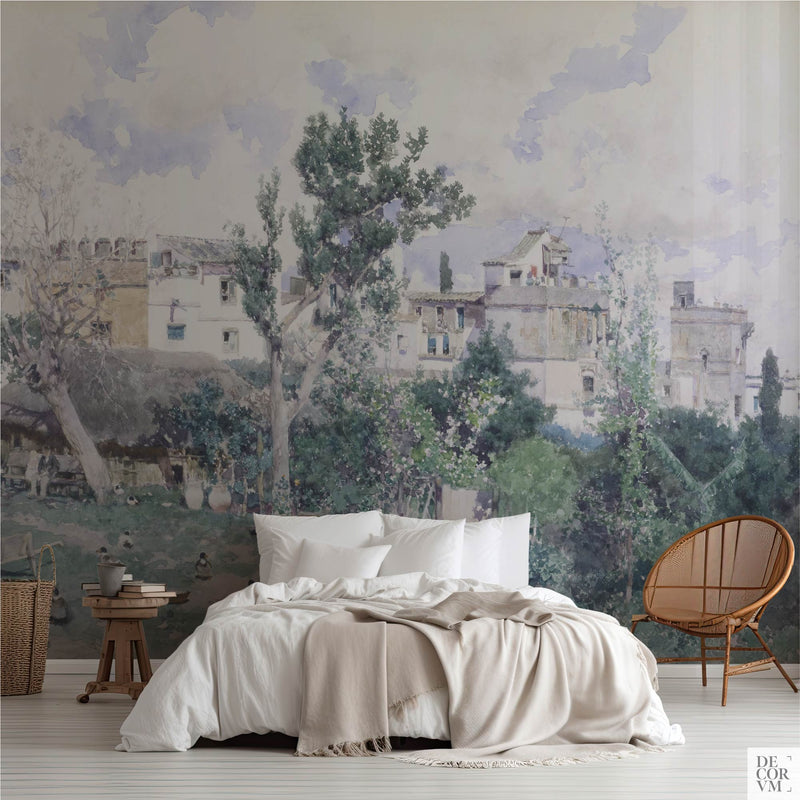 Spanish garden courtyard wallpaper mural of a Seville kitchen garden in soft watercolor, covering the wall behind a low bed with white linens, a wooden stool and a round rattan chair in a soft-neutral bedroom by Decorvm.