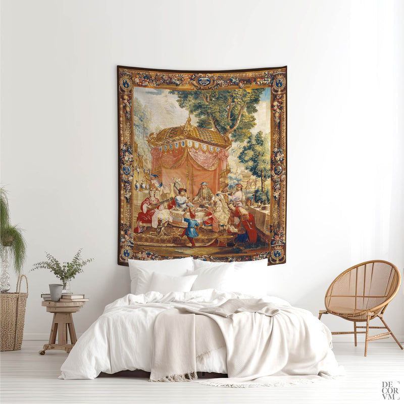 Large traditional Chinoiserie wall tapestry hung as a grandmillennial fabric art statement piece above a bed with white linens, paired with a rattan chair in a bright bedroom.