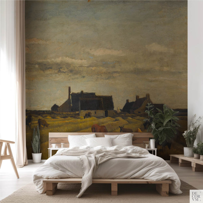 Vintage pastoral landscape wallpaper mural spanning the wall behind a low wooden bed with white linens, potted greenery, and a sheer curtain in a soft-neutral bedroom by Decorvm.
