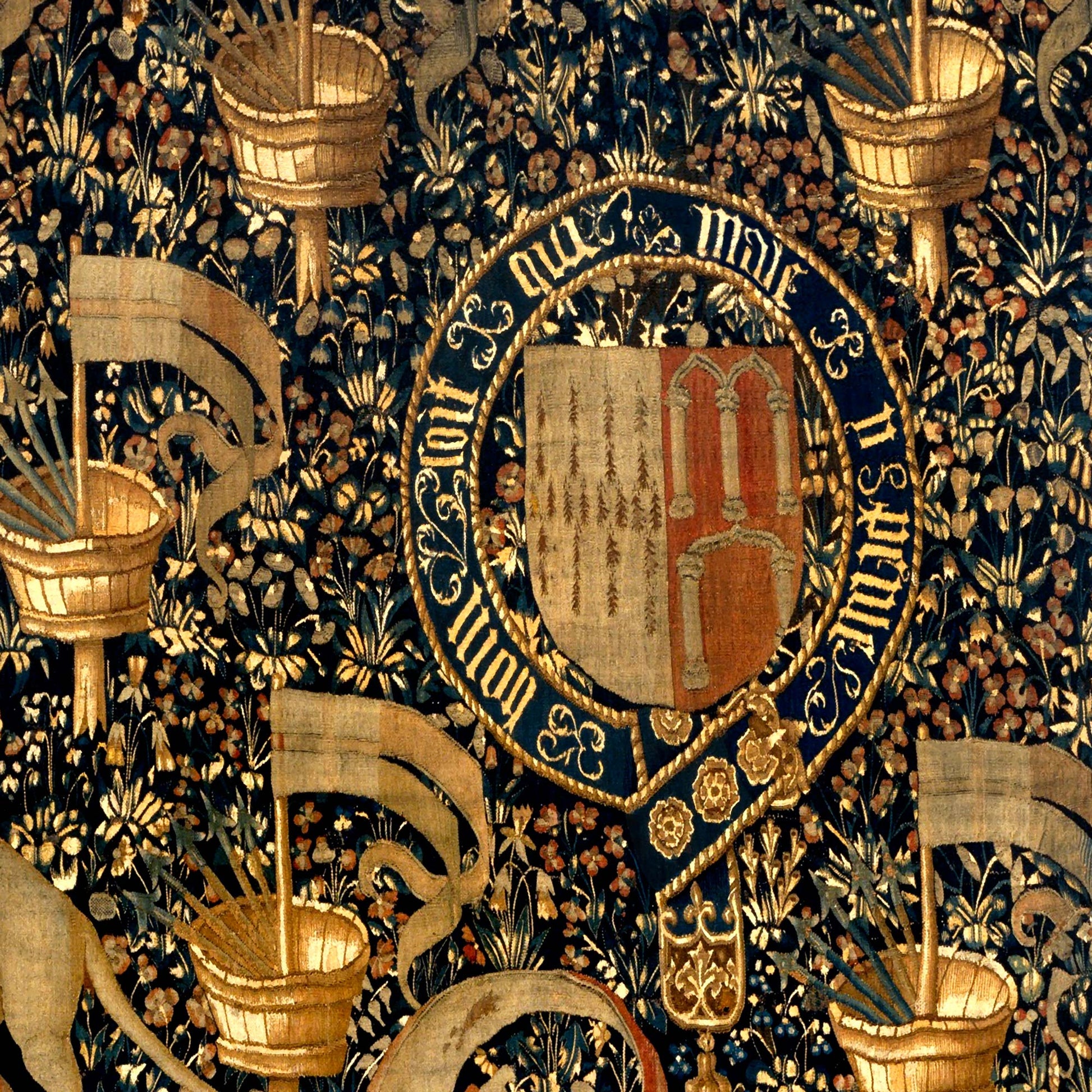 Close-up of medieval coat of arms encircled by golden text and surrounded by banners and flowers.