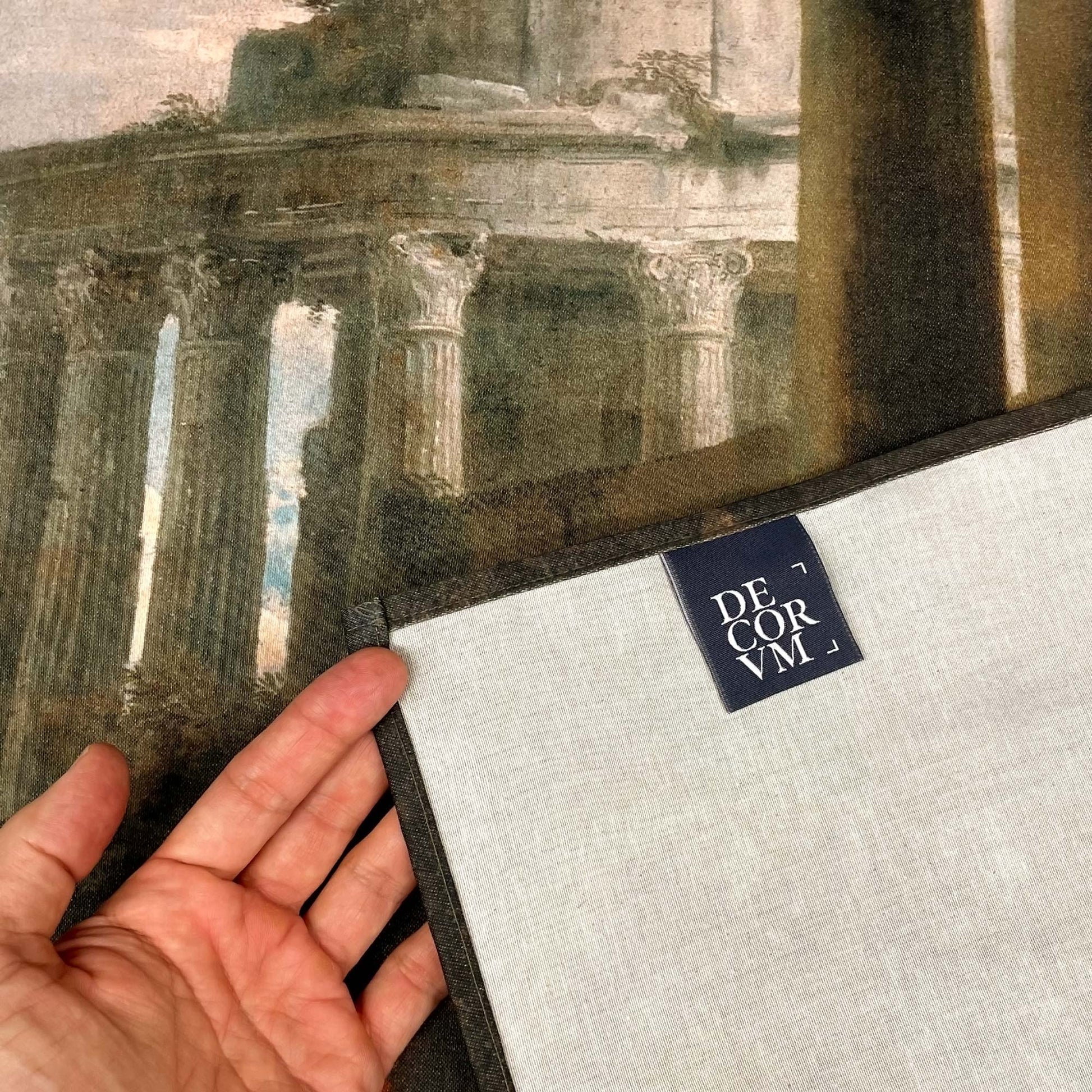 Close-up of tapestry fabric and stitching showing corner fold, label with Decorvm logo, and fine print quality.