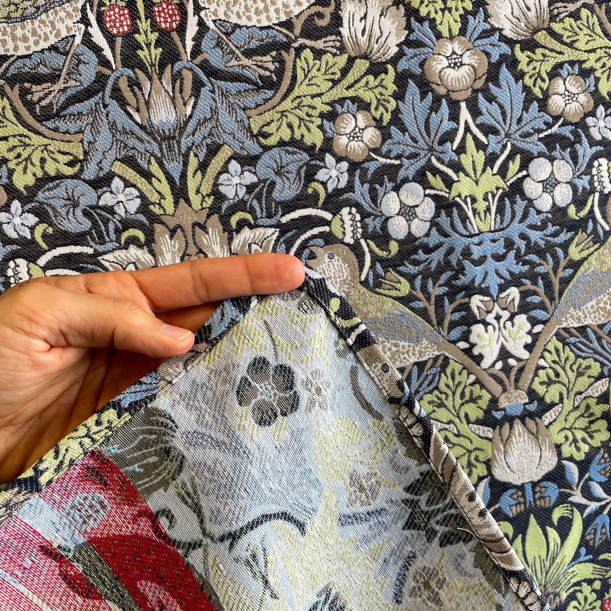 Back side and hem detail of woven jacquard Strawberry Thief tapestry showing finished edges and fabric thickness.