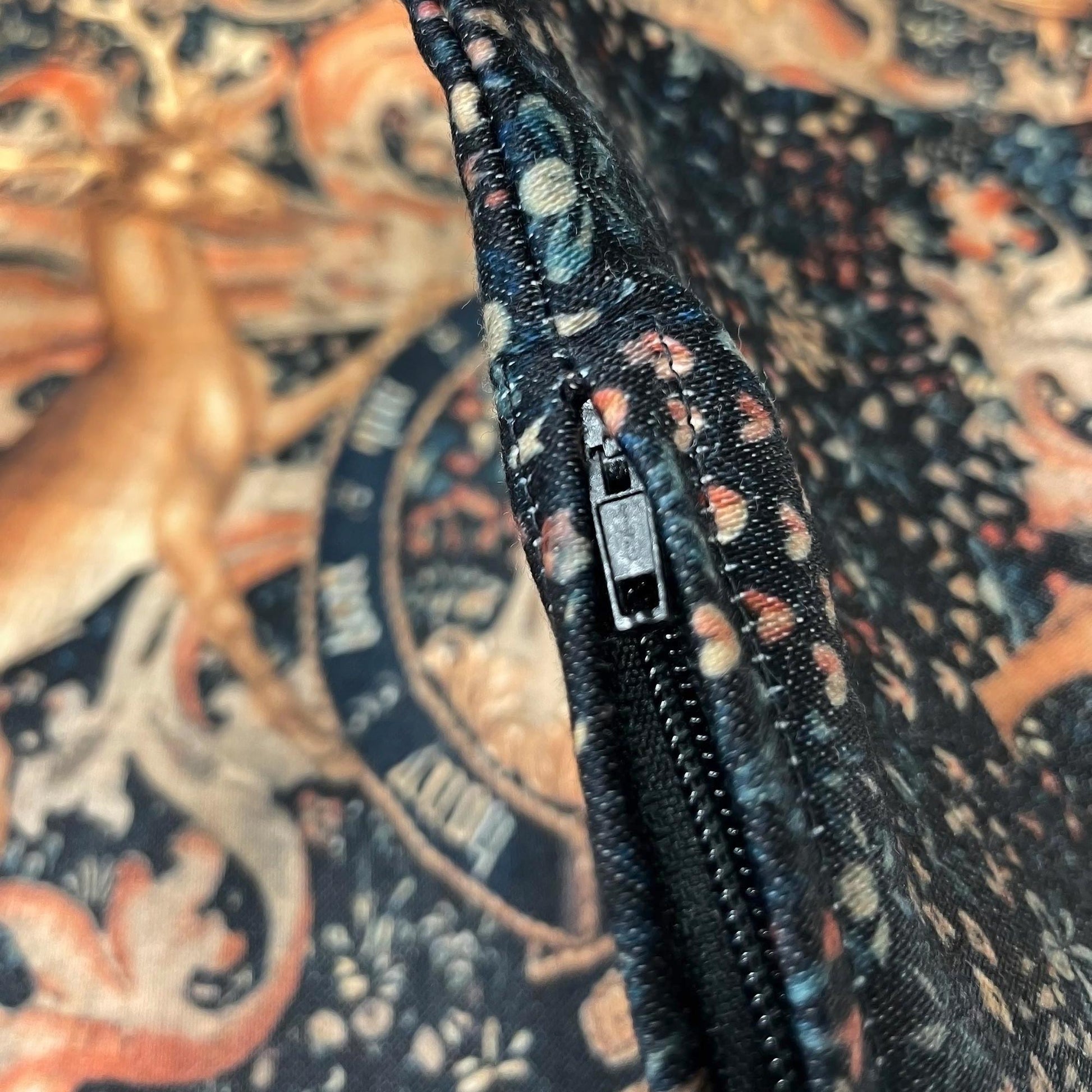 Macro view of the discreet black zipper pull and durable stitching on the Medieval Heraldry cushion cover.