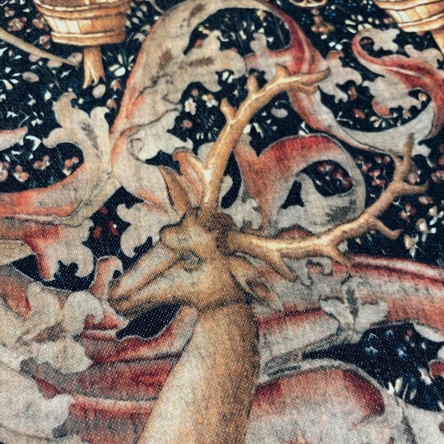 Close-up of a noble stag's head and majestic antlers surrounded by a moody millefleurs background — design detail from the medieval Lord Dynham tapestry.