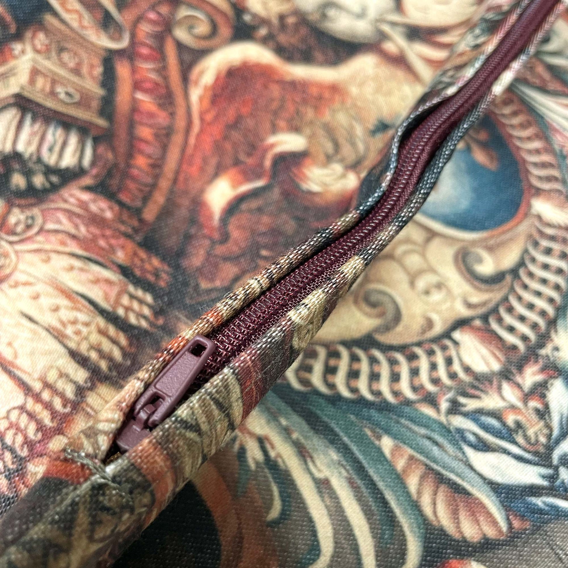 Close-up of the dark burgundy zipper closed along the seam of the Portière Chariot of Triumph cushion cover.