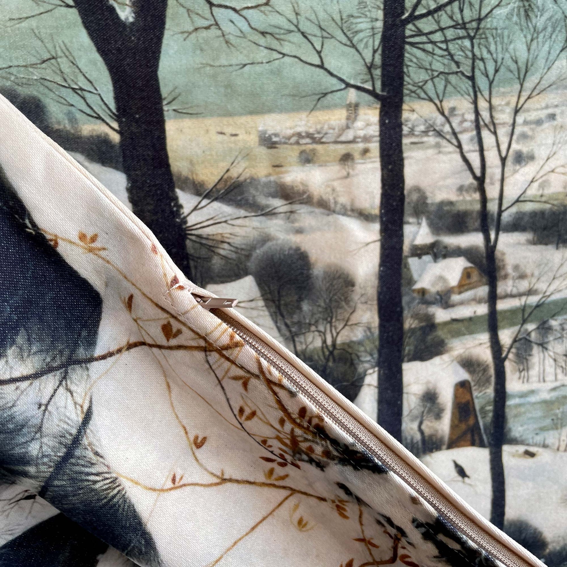 Close-up of “Hunters in the Snow” throw pillow cover showing hidden zipper and soft textured fabric, winter village print in sage and ivory.