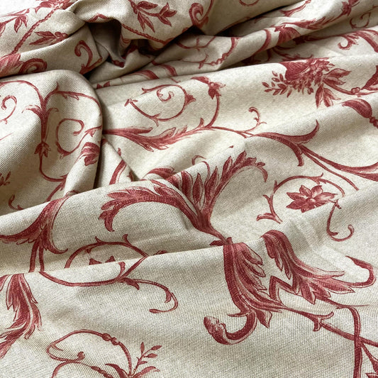 Softly folded upholstery fabric displaying a classic crimson red acanthus leaf and botanical motif over a neutral beige background.