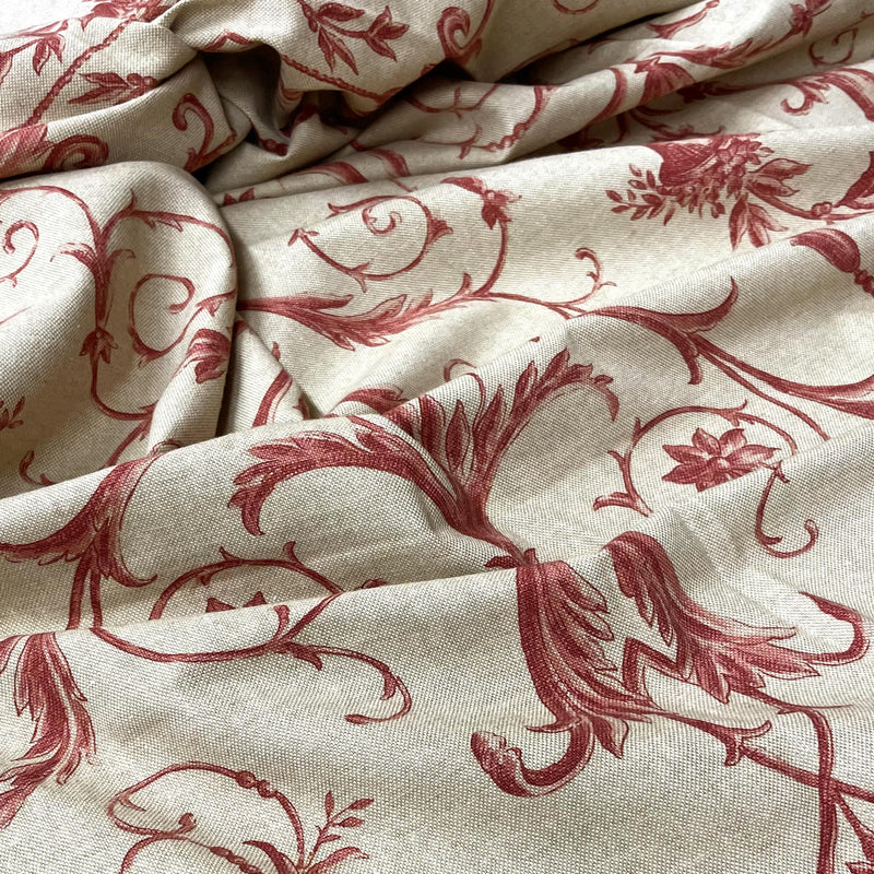 Softly folded upholstery fabric displaying a classic crimson red acanthus leaf and botanical motif over a neutral beige background.