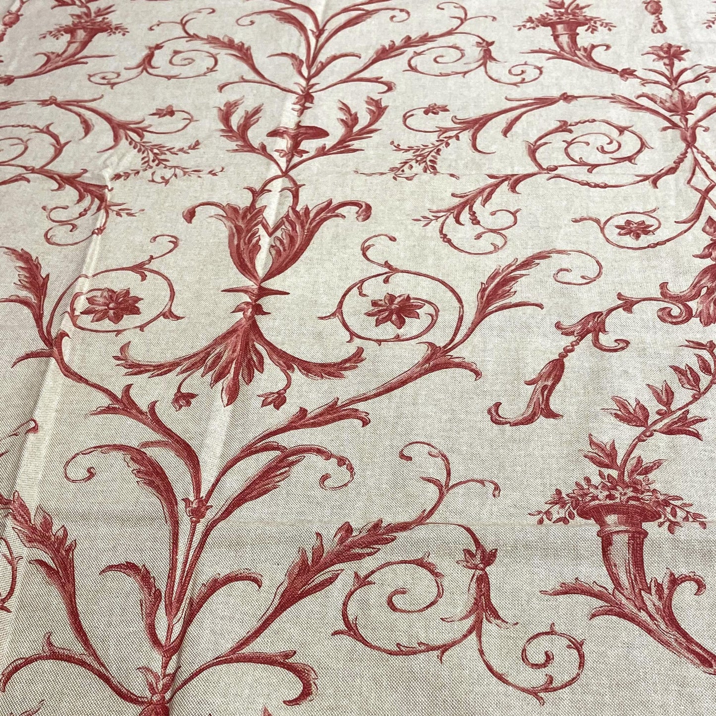 Overhead view of a traditional fabric pattern featuring sweeping red acanthus vines, florals, and stylized urns on a light linen-colored ground.