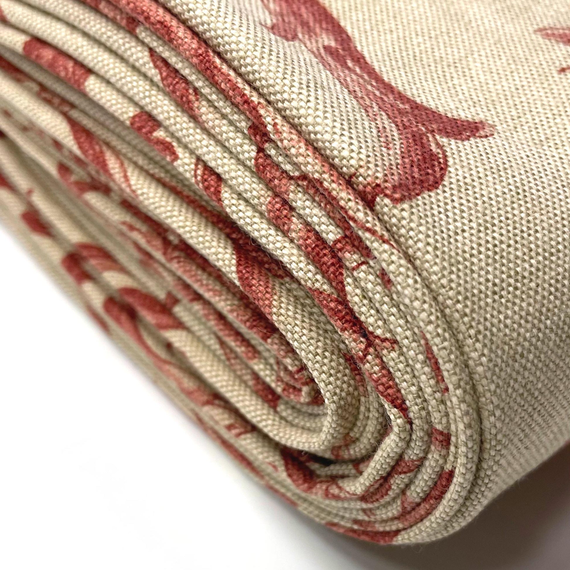 Heavy rolled bundle of upholstery fabric showcasing the layered edge of the textile and the repeating crimson red botanical print.