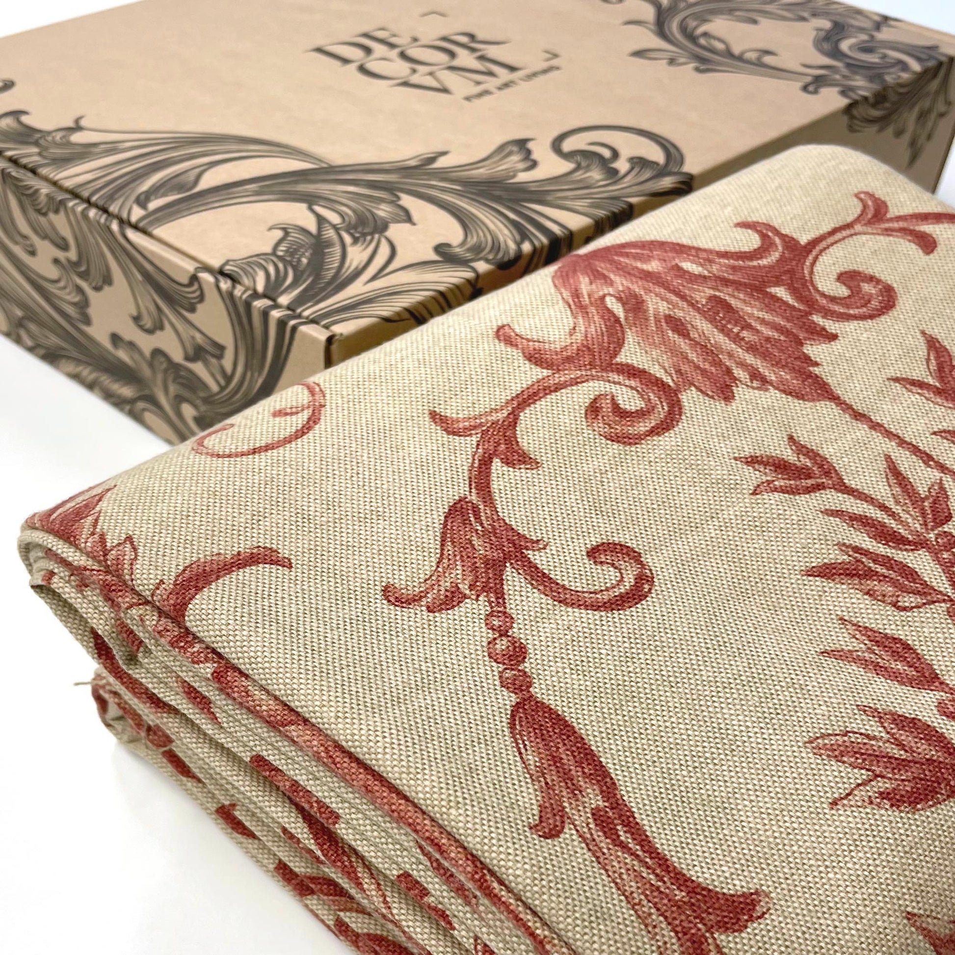Elegantly folded crimson acanthus fabric placed beside a custom kraft cardboard box bearing the Decorvm Fine Art Living logo and black damask details.