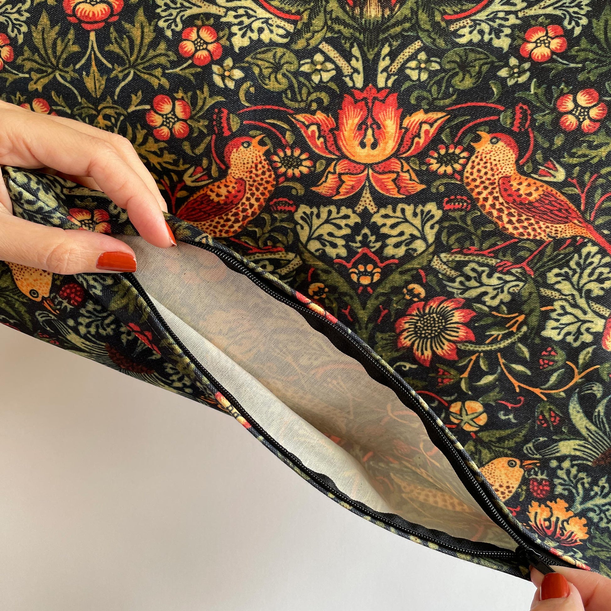Hands opening the zipper of the dark green Strawberry Thief pillow cover, revealing the white inner lining.