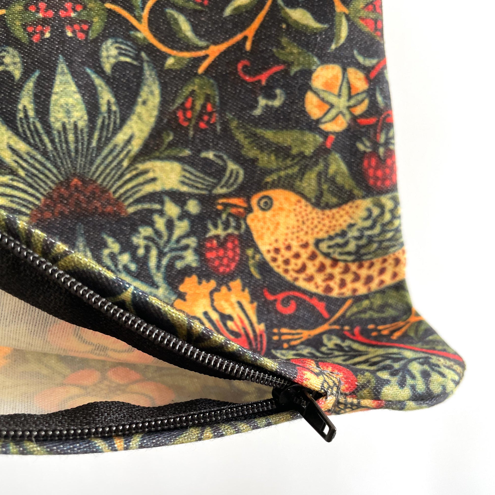 Closed zipper pull on the William Morris Strawberry Thief pillow cover in dark green.