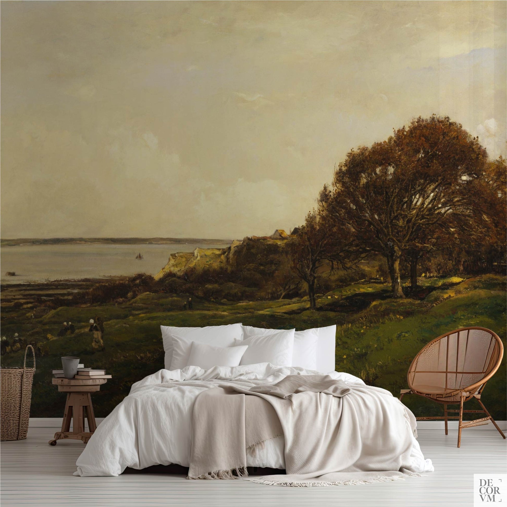 French seaside landscape wallpaper mural in a coastal bedroom with white bedding and rattan chair — vintage painting of green rolling hills, autumn oak trees, and calm sea with sailboats