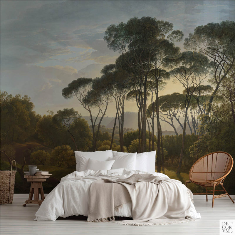 Italian landscape with umbrella pines wallpaper mural in a bedroom with white bedding, wooden side table, and rattan lounge chair.