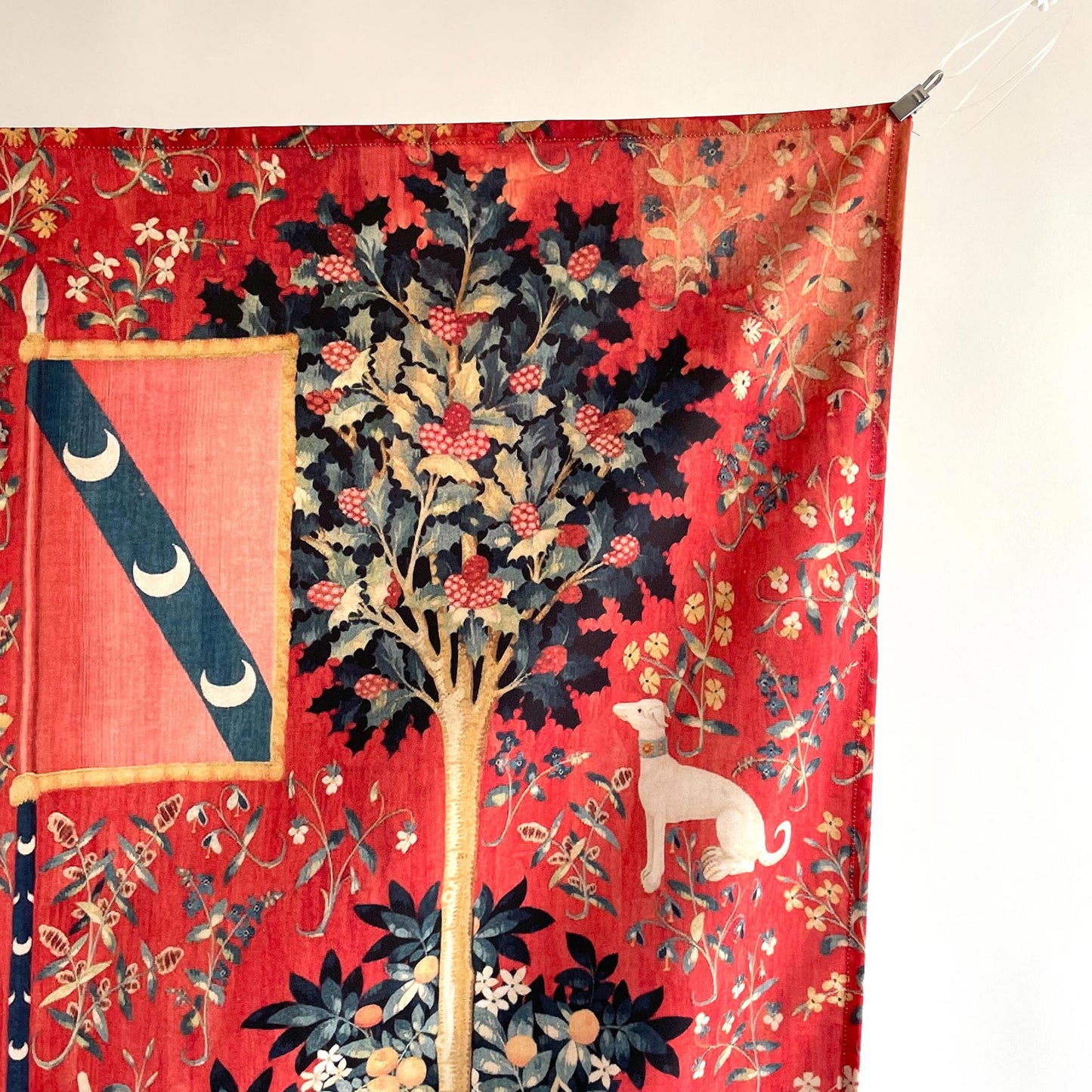 Top-right detail of the Lady and the Unicorn tapestry showing a flag with three crescent moons, a central holly tree, a white greyhound with collar, and delicate floral details.