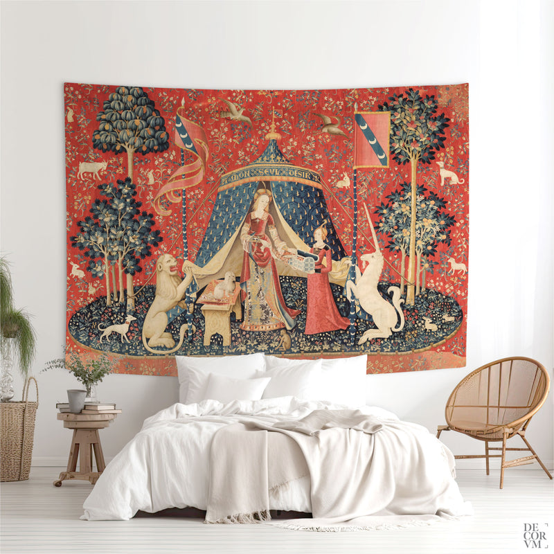 Large Lady and the Unicorn medieval tapestry hung above a bed in a bright boho-chic bedroom with a wicker chair and potted plants.