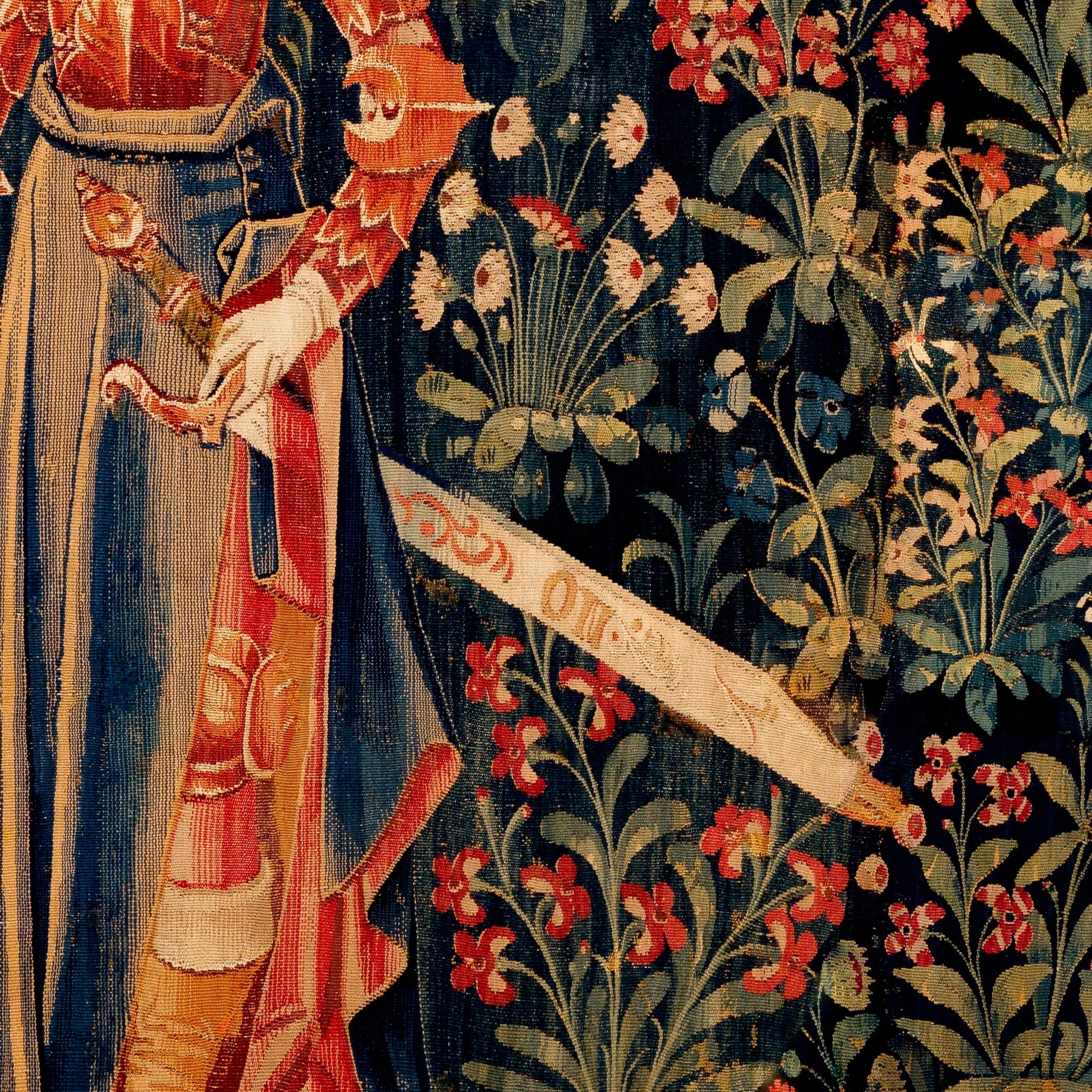 Inscribed ceremonial sword and gold-trimmed crimson skirt against a navy botanical ground with red blooms — detail of the late 15th-century Flemish millefleurs Penthesilea tapestry.