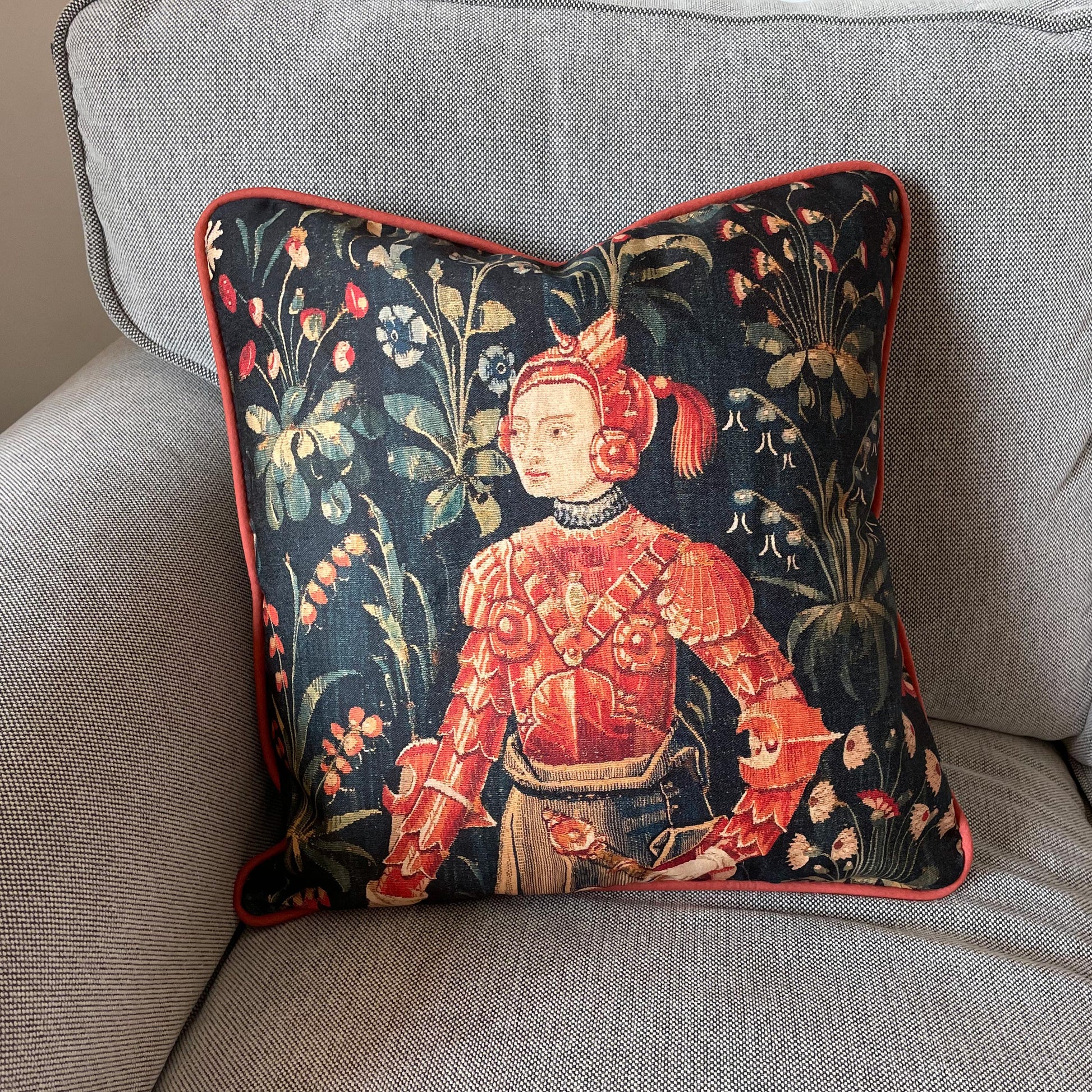 Medieval Amazon Queen Penthesilea cushion styled on a light grey textured sofa — dark academia decor with red corded edge piping.