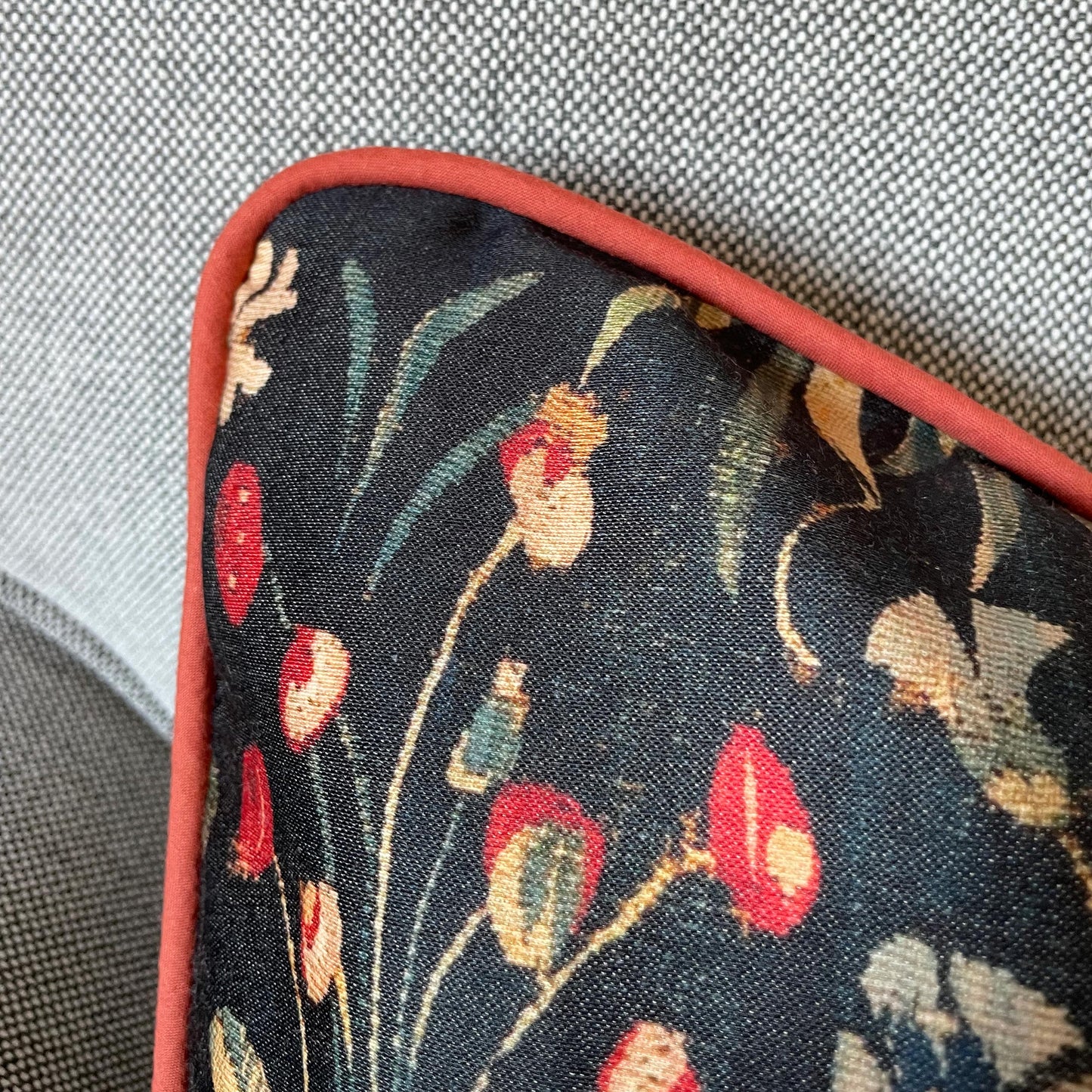 Close-up of the dark floral millefleurs pattern and tailored red corded edge — design detail from the medieval Amazon Queen cushion cover.