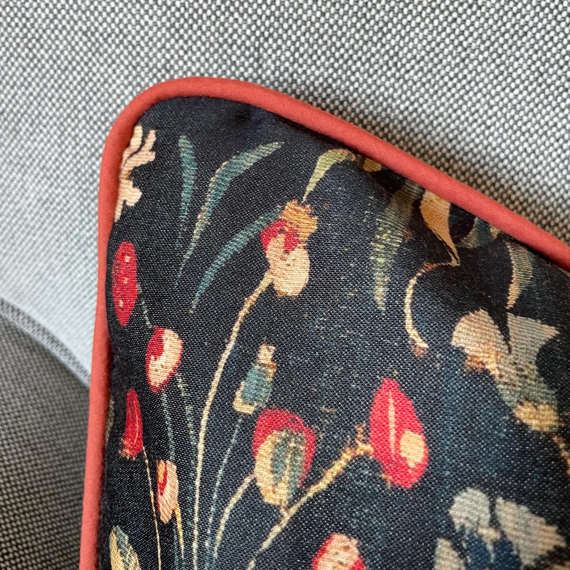 Close-up of the dark floral millefleurs pattern and tailored red corded edge — design detail from the medieval Amazon Queen cushion cover.