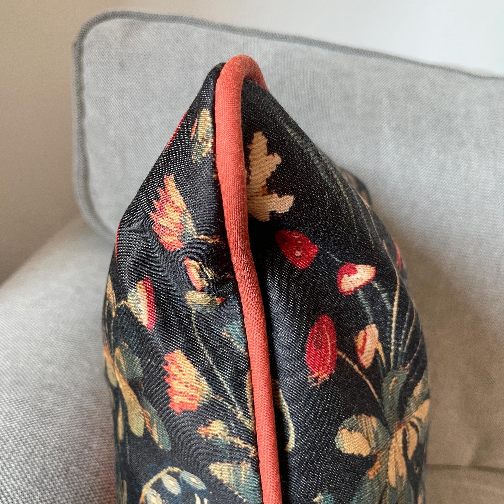 Side profile of the Medieval Amazon Queen cushion cover, showing the plush insert, woven medieval floral design, and red piping finish.