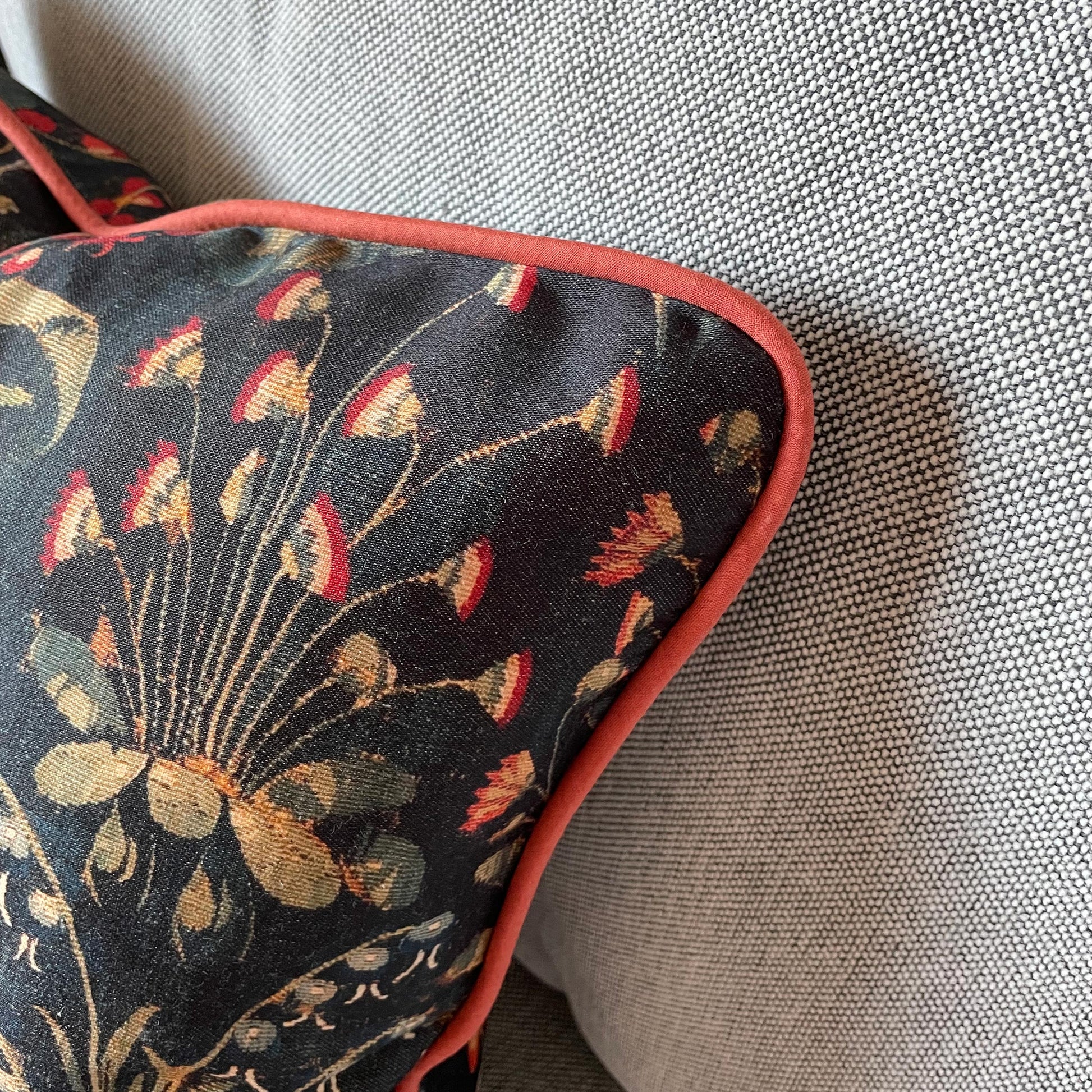 Macro close-up of the millefleurs tapestry print framed by the red corded edge — design detail from the Medieval Amazon Queen cushion cover.