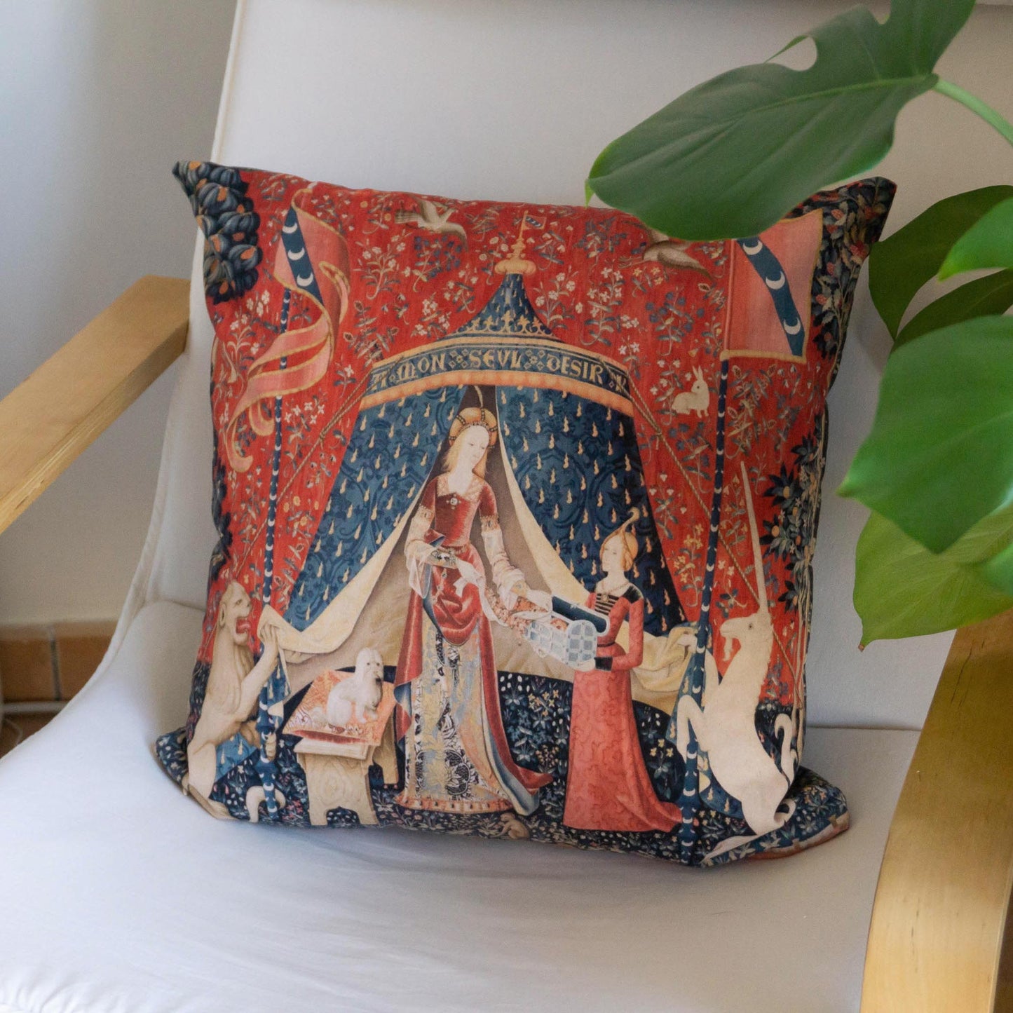Lady and the Unicorn medieval cushion cover styled on a modern wooden armchair beside a green plant — maximalist dark academia decor.