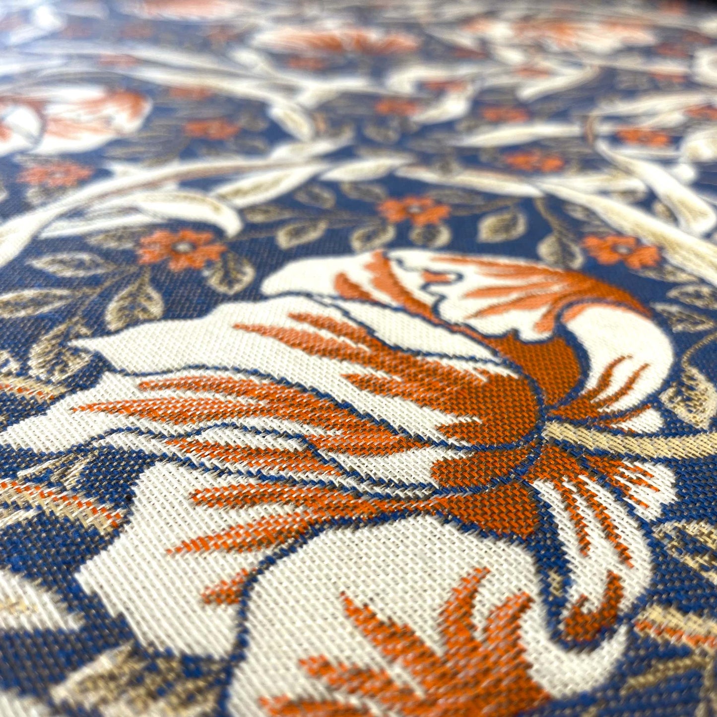 Extreme close-up macro shot of the fabric's jacquard weave, highlighting the textured, interlocking threads of a single rust and white flower on the blue background.
