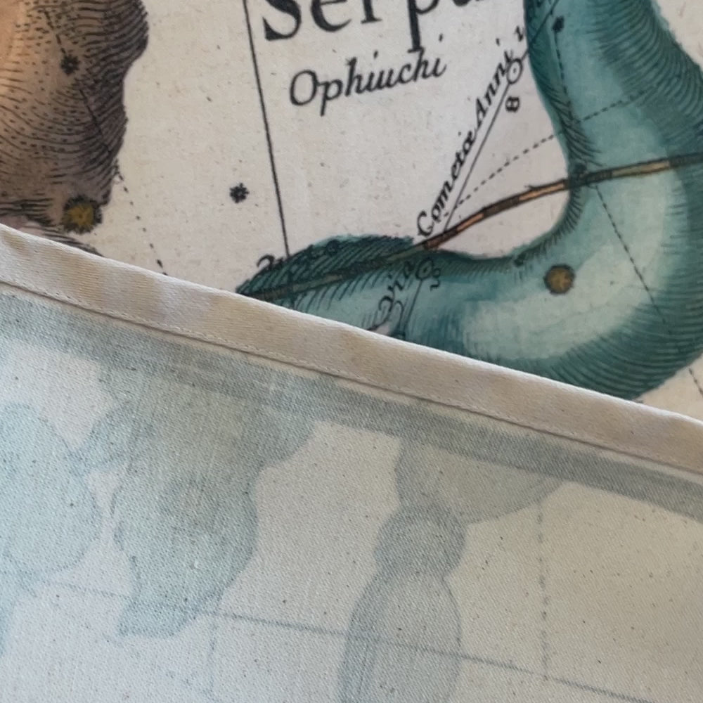 A video demonstration of an antique constellation map wall tapestry. It starts with a close-up of a hand showcasing the neatly stitched hem and durable cotton blend fabric, then slowly pans outward to reveal the full 1693 celestial star chart, highlighting vibrantly detailed mythological figures like Serpentarius, Hercules, and Aquila.