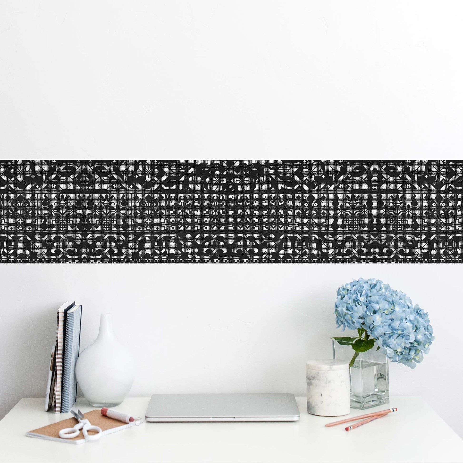 Renaissance geometric peel and stick wall border in black — home office desk with laptop, notebooks, and blue hydrangea vase against white wall
