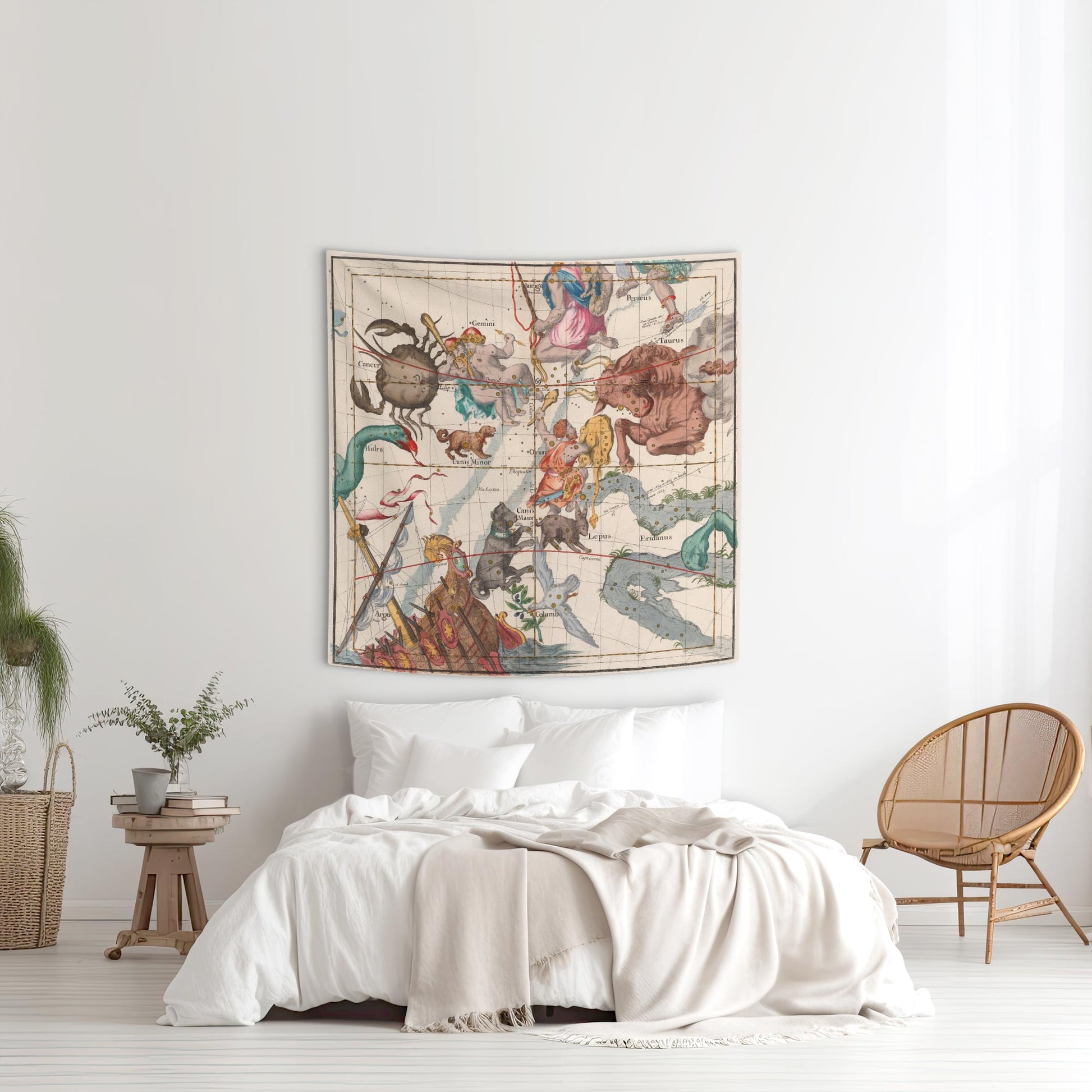 Orion and Taurus vintage star chart tapestry displayed above a white bed with a wicker chair nearby in a bright bedroom.