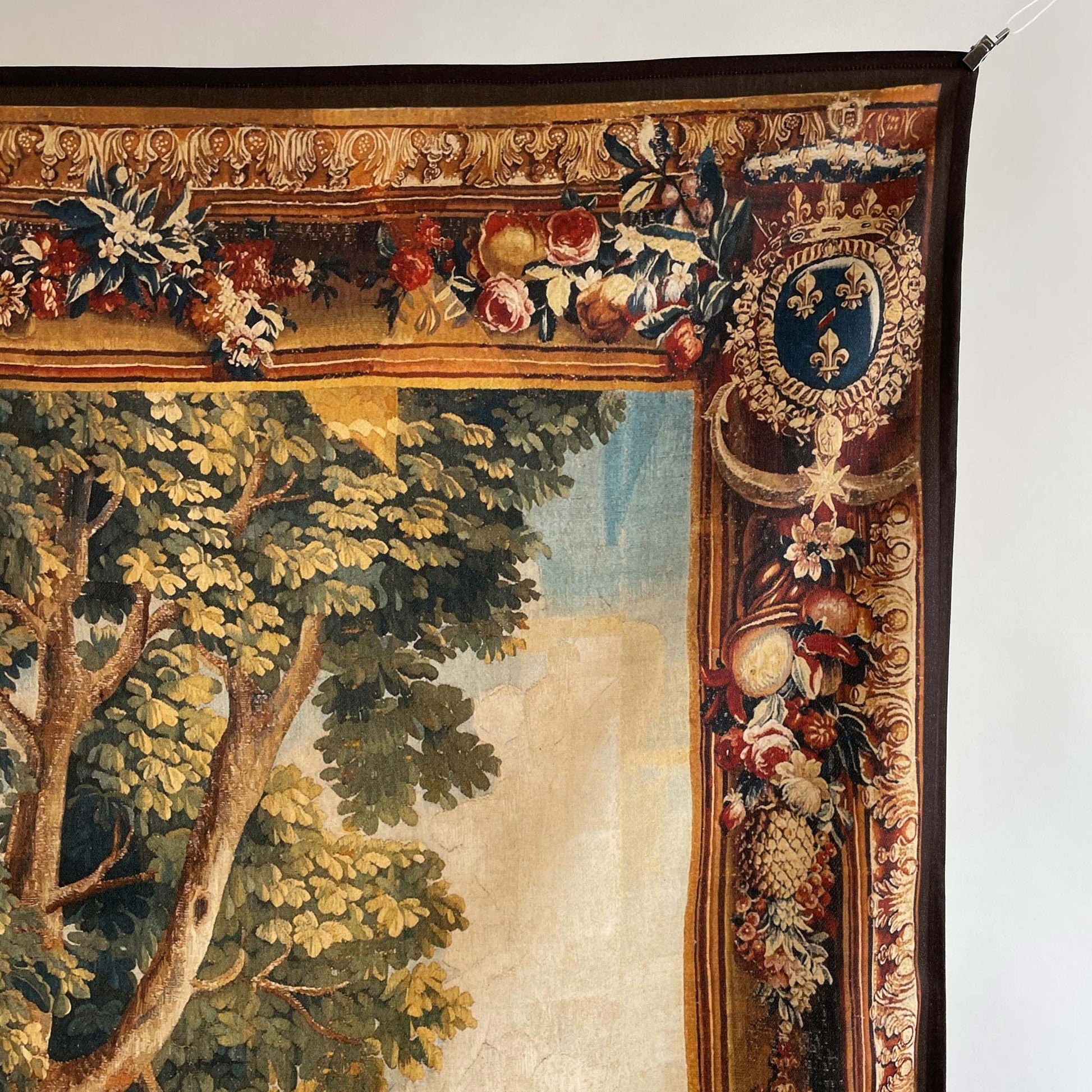 Close-up of the ornate floral border and French fleur-de-lis crest on the traditional Chinoiserie wall tapestry, highlighting the rich woven details of the lush green tree foliage.