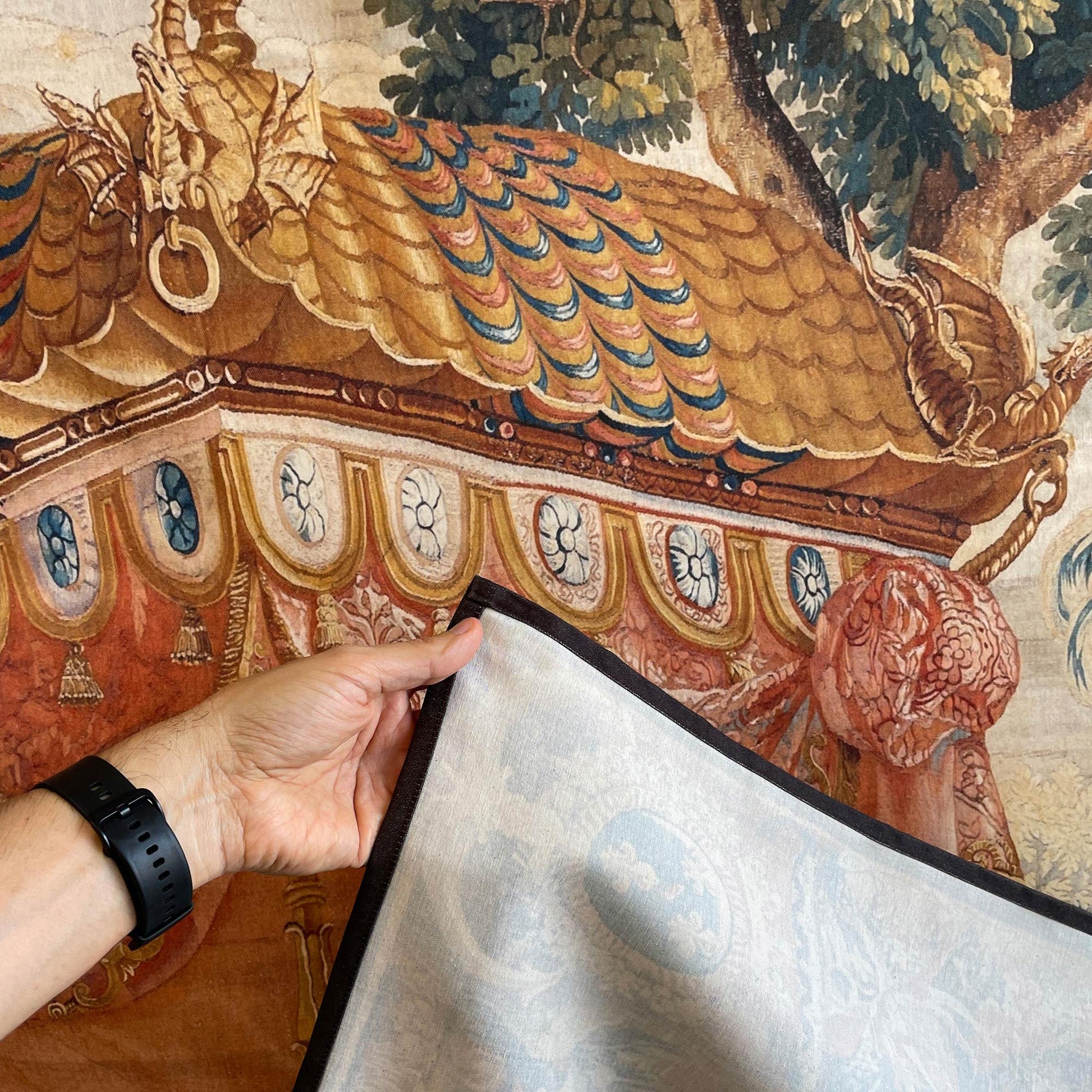 A hand holding the corner of the elegant fabric art tapestry to reveal its high-quality woven backing, with the intricate Chinoiserie pavilion canopy design visible in the background.