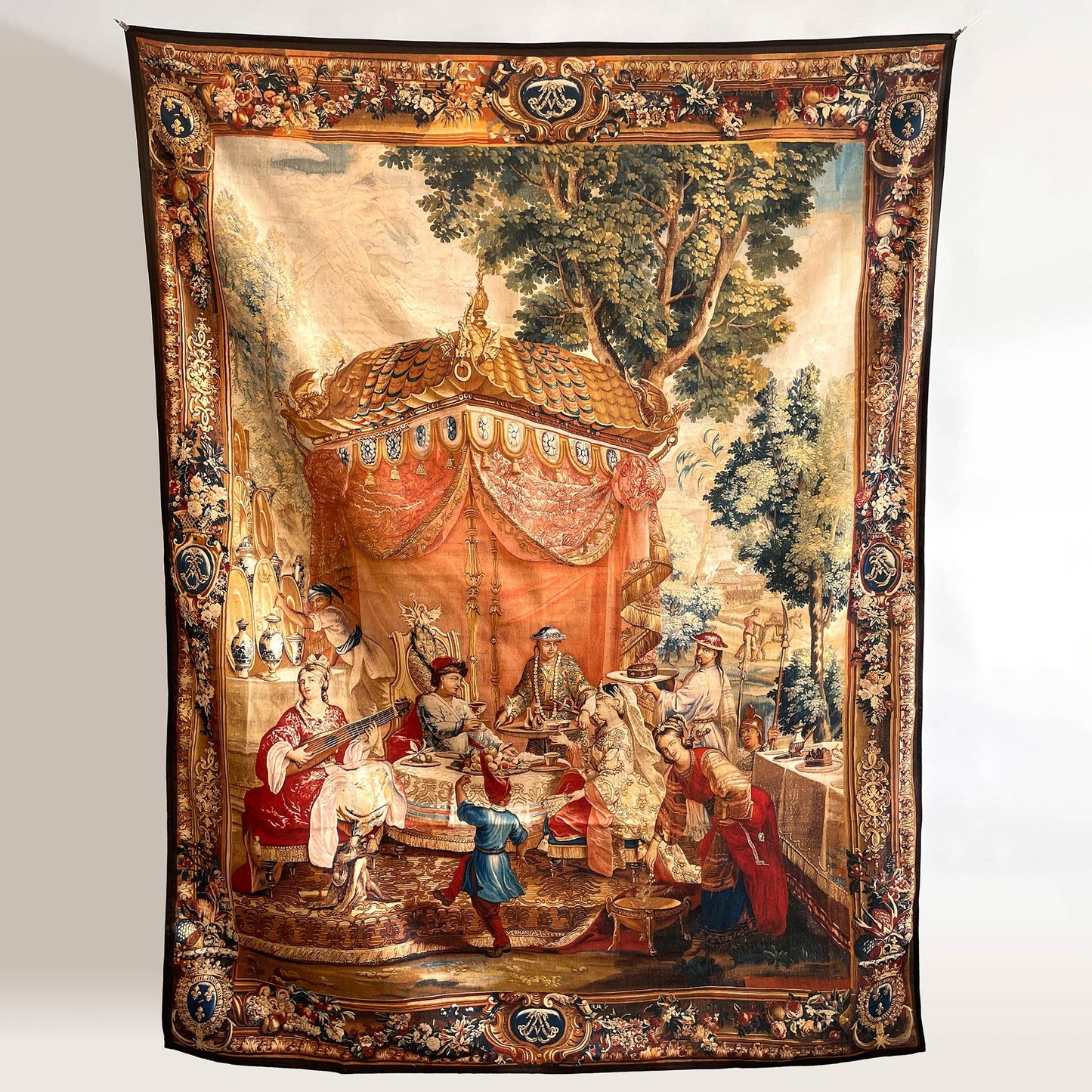 Full studio view of the traditional Chinoiserie wall tapestry hanging against a white background, displaying the complete 17th-century royal banquet scene and its ornate decorative borders.