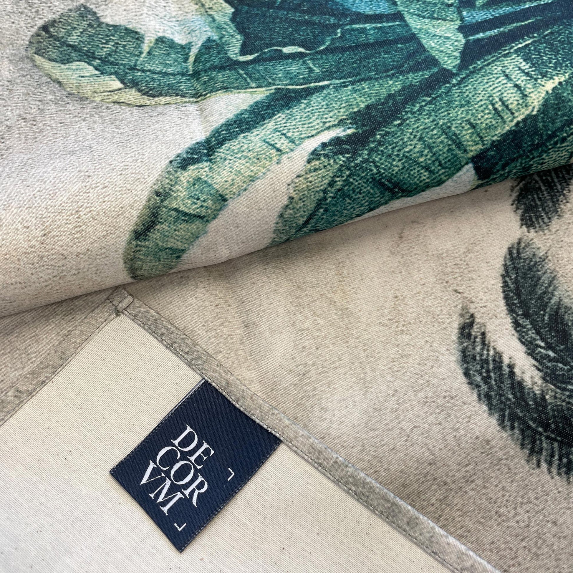 Close-up of the vintage exotic jungle wall tapestry fabric folded over, showing the printed tropical palm leaves and the sewn edge with a Decorvm brand tag.