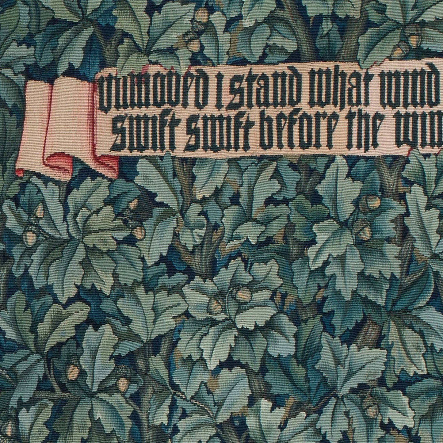 Detail of woven oak leaves and acorns with a banner reading 'Unmoved I stand' on a dark blue-green background — Greenery tapestry typography detail.