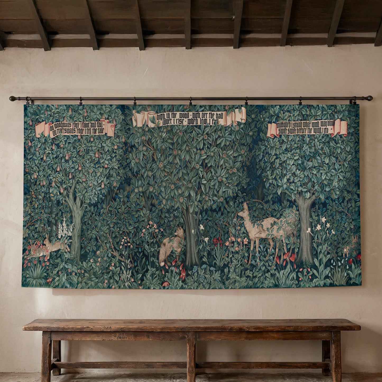 Large William Morris Greenery wall tapestry hung on a textured plaster wall beneath exposed wooden ceiling beams, displayed over a long rustic wooden bench — Arts and Crafts forest with deer, a fox, and botanical detail.