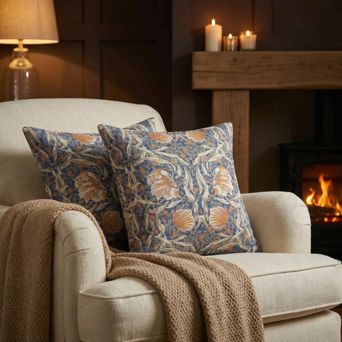 William Morris Pimpernel jacquard throw pillows on a cream armchair beside a fireplace — woven blue and rust 1876 Arts and Crafts pattern by Decorvm.